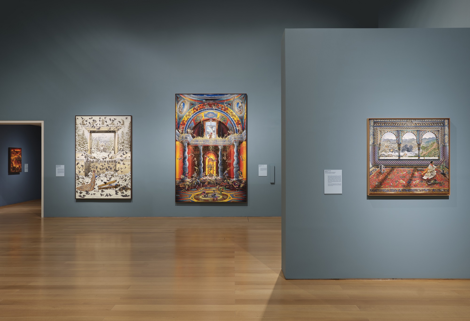 An exhibition room with blue walls and brightly coloured paintings hung on the walls. It is the exhibition of Raqib Shaw: Ballads of East and West, Hostetter Gallery, February 6 - June 4, 2024.